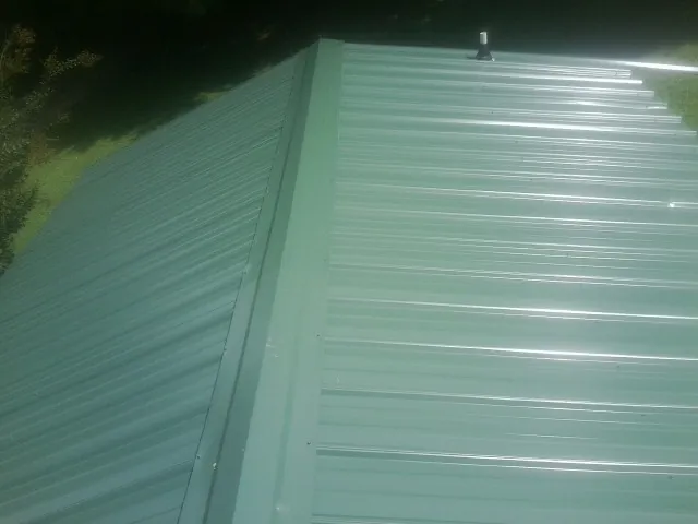 New green metal panels meeting at the ridge of a roof — Flat Roof Repair work by our crew in Irving