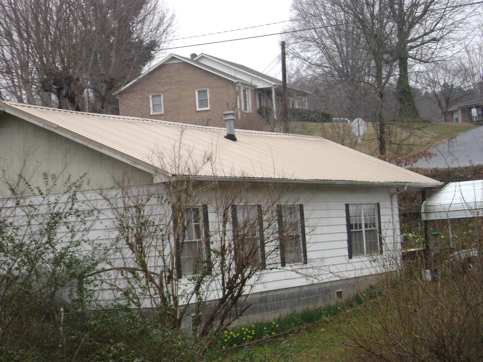 Tan metal roof on a white sided house set into a hillside — Commercial Roofing by Roofing Brothers in Irving